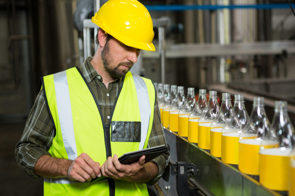 Serious male worker using digital tablet in juice factory