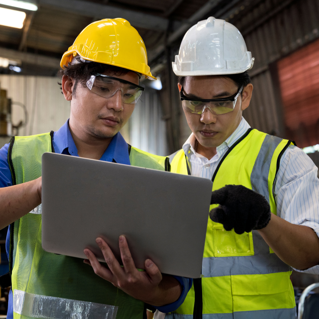 two men discussing something on a laptop in a warehouse