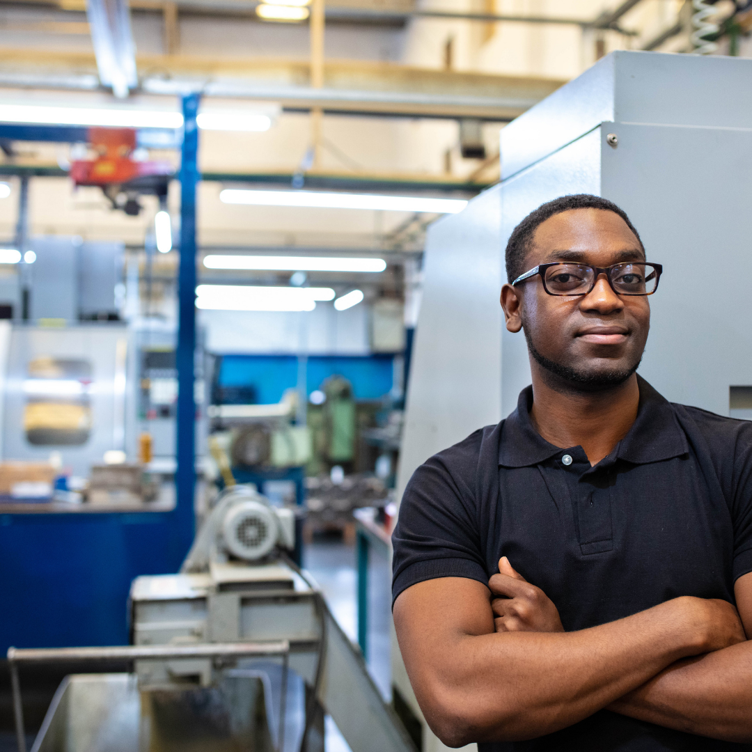 african american man smiling with a machine in the background inside a manufacturing facility