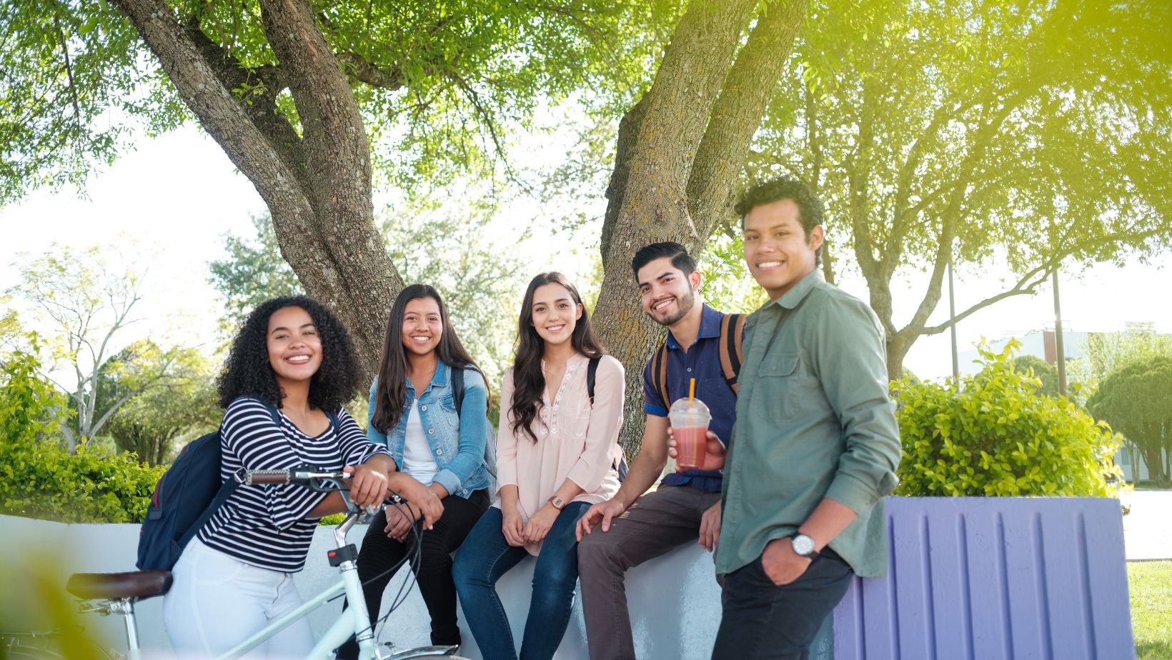 group of 5 diverse millennials outside in a park smiling at the camera