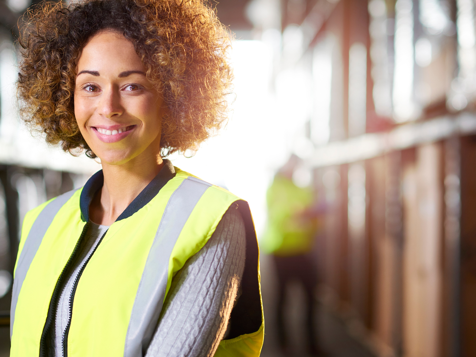 african american woman in a bright colored vest standing in a warehouse smiling
